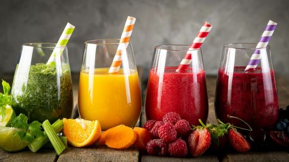 Four different smoothies with the fruit scattered in front of the glasses