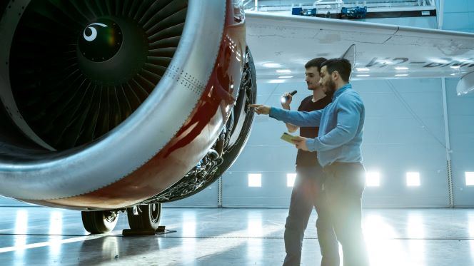 In a Hangar Aircraft Maintenance Engineer Shows Technical Data on Tablet Computer to Airplane Technician, They Diagnose Jet Engine Through Open Hatch