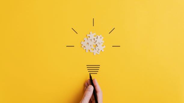 Person drawing lightbulb with puzzle pieces