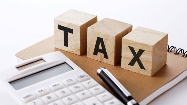 three wooden blocks with the word T A X on them alngside a calculator and pen