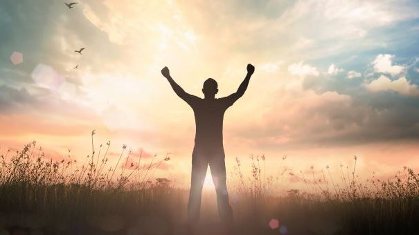 Person standing with arms in the air under sunrise