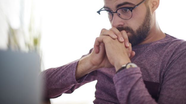 Man waiting infront of a laptop, clenching his hands in anticipation