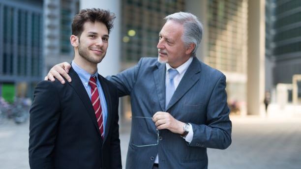 Older employee with arm round younger employee