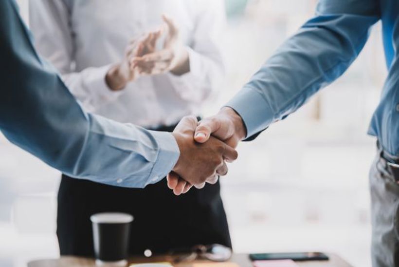 Two people in shirts shaking hands over a desk