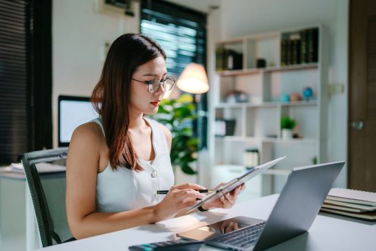 Woman At Desk With Clipboard And Laptop